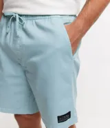 Bermuda celeste de sarga con cintura elástica ajustable con cordón, bolsillos laterales y traseros, y etiqueta con logo en la parte inferior.