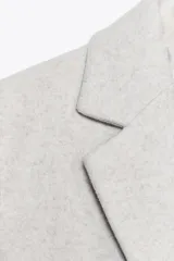 Abrigo gris de cuello solapa y manga larga. Tiene bolsillos de vivo en el delantero, forro interior combinado a tono y cierre frontal con botones.