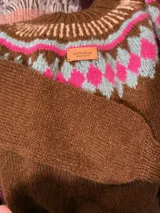 Sweater marrón tejido a mano en mohair con cuello redondo y diseño con motivos geométricos en colores blanco, rosa y celeste.