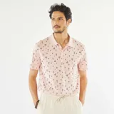 Remera polo de piqué de algodón color rosa con estampado de palmeras y tablas de surf en negro.