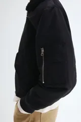 Campera bomber de nylon color negro con corte holgado y levemente acolchada. Cuenta con cuello de peluche al tono, cierre frontal metálico, bolsillos laterales con solapa y un bolsillo con cierre en la manga. Posee puños y bajo acanalados.