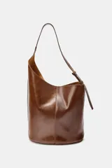 Bolso marrón de cuero, formato saca asimétrica. Tiene asa de hombro ajustable y cierre con imán. Incluye una cartera con bolsillo extraíble.