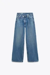 Pantalón de jean celeste de tiro alto, corte wide leg y largo hasta el tobillo. Presenta un diseño asimétrico en la cintura con cierre frontal cruzado con cremallera y botones metálicos.