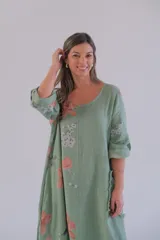 Vestido largo verde con estampado floral en tonos rosados y blancos, mangas 3/4 con ajuste de botón y ruedo irregular.