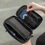 Riñonera negra con correa ajustable, confeccionada en material impermeable xPac X21. Cuenta con 7 bolsillos internos y 2 externos, organizador con apertura de 180°, espacio para cables y cargadores, detalles en color ladrillo y cierres impermeables.