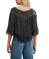 Blusa blanca de poliéster con detalles de encaje en el escote en V, en los puños de manga 3/4 y en el ruedo inferior. Presenta pinzas verticales en el frente y botones frontales.