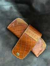 Estuche para lentes color borgoña con textura símil cocodrilo y cierre con broche a presión.