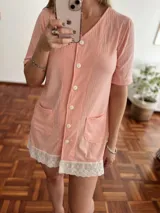Camisola corta color salmón con botones frontales, bolsillos y detalles de encaje blanco en el ruedo.