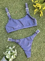 Conjunto de bikini azul con corpiño de breteles finos y hebillas metálicas en los tirantes. La bombacha es colaless y también tiene hebillas metálicas en los laterales.