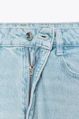 Pantalón de jean gris oscuro, de corte mom fit, tiro alto y largo tobillero. Cuenta con cinco bolsillos, cierre frontal con cremallera y botón.