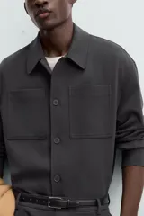 Sobrecamisa negra de corte amplio, con cuello solapa, manga larga con puños abotonados, bolsillos de parche en el pecho, bolsillos laterales y cierre frontal con botones.