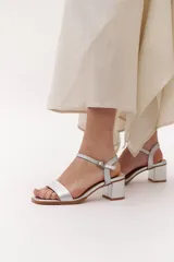 Sandalias plateadas de cuero con taco bajo cuadrado y tira fina con hebilla en el tobillo.