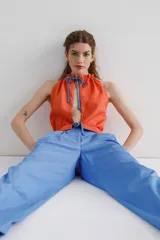 Top sin mangas color naranja con abertura en el delantero y espalda. Detalle de fruncido en el cuello y ruedo que se ajusta y cierra con lazo en contraste color azul.