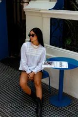 Camisa color crema con cuello alto y mangas largas con volados en los puños. Presenta detalles de crochet y broderie en el frente.