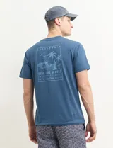 Remera verde con estampado en la espalda de una playa con palmeras y la frase "Ride the waves".