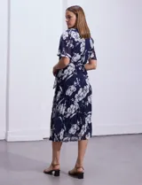 Vestido largo de gasa estampada con flores blancas sobre fondo azul marino, marca Sandra Darren. Tiene escote en V cruzado, cintura elastizada con lazo de ajuste, falda plisada y forro interno a tono.