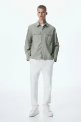 Sobrecamisa verde oliva de corte recto, con cuello inglés, cierre frontal con botones a presión y dos bolsillos de parche con solapa en el pecho.