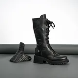 Borcego de cuero vacuno color negro, con suela de goma artesanal, caña alta con aplique capitoneado desmontable y horma de punta redonda.