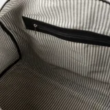 Bolso de viaje tipo duffel de cuero negro con doble asa de mano y correa de hombro ajustable.