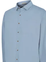 Camisa celeste de manga larga con cuello camisero, cierre con botones de madera y bolsillo en el pecho.