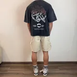 Remera negra con efecto gastado, corte boxy y estampado en la espalda con un logo abstracto en marrón, cadenas blancas, colmillos y texto "Midway Studios Buenos Aires".