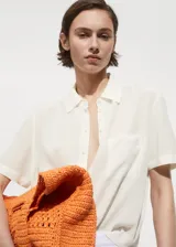 Camisa color crema de tejido fluido, manga corta, cuello camisero y cierre frontal con botones.