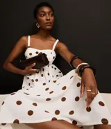 Vestido midi evasé sin mangas, confeccionado en tejido airflow color blanco con estampado de lunares marrones. Presenta escote corazón, breteles anchos con elásticos y lastex en la espalda.