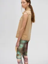 Camisa sin mangas de denim liviano color camel, con cuello camisero y botones frontales. Presenta bordados temáticos marinos en el pecho, incluyendo un sol, olas, una gaviota y vida marina.