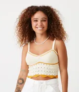 Top cropped de punto color crema con detalles de rayas contrastantes en color mostaza. Presenta escote en V, tirantes finos regulables y un diseño texturizado con calados. El bajo es festoneado y ondulado.