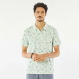 Remera polo verde claro con estampado de palmeras y tablas de surf en negro.