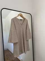 Vestido de tejido de punto a rayas horizontales beige y blanco, con escote en V y mangas acampanadas de tres cuartos.