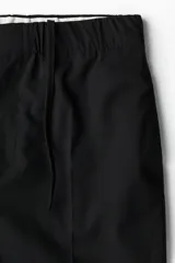 Pantalón negro de corte relajado, con cintura elástica ajustable con cordón, cierre con botón y corchete, bolsillos laterales y traseros.