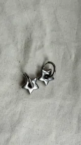 Par de aros plateados de acero quirúrgico con forma de estrella colgando de un aro.