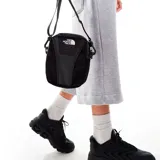 Bandolera negra de poliéster con detalles en cuero sintético. Tiene correa ajustable, cierre superior con cremallera, bolsillos internos y gancho para llaves. El logo de The North Face está estampado en blanco en el frente.