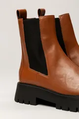 Bota Chelsea color verde militar de cuero, con elásticos laterales negros, tirador trasero y suela track negra.