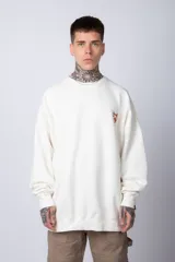 Buzo color crema de corte oversize confeccionado en tela friza con cuello redondo y puños y cintura acanalados. Presenta un pequeño bordado en el frente y un estampado grande en la espalda.