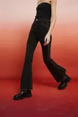 Pantalón jean negro de tiro alto, corte flare con tajo en el ruedo y detalles de tachas metálicas a los costados.