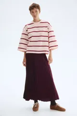 Remera de manga tres cuartos con cuello redondo, hombros caídos y corte holgado. Presenta un patrón de rayas horizontales en tonos rosa pálido, blanco y granate.