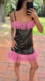 Vestido corto de lentejuelas negras con escote recto y tirantes finos. Presenta detalles de flecos de rafia en color beige tanto en el escote como en el ruedo.