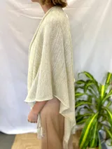 Ruana tejida color crudo con hilos dorados y flecos.