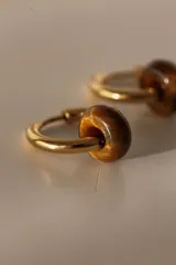 Par de aros tipo argolla dorados con dije de piedra natural con patrón de manchas negras sobre fondo blanco.