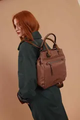 Mochila bandolera color marrón con herrajes color peltre. Tiene un compartimento principal amplio con cierre, un bolsillo frontal con cierre y dos bolsillos laterales abiertos. Incluye correa ajustable para usar al hombro o cruzada.