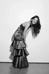 Falda larga color marrón con textura brillante, corte ajustado en la cintura y falda con volados en capas y tajo lateral.