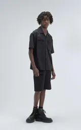 Camisa negra de manga corta estilo técnica, confeccionada en microfibra liviana. Tiene doble bolsillo frontal con cierre de cremallera y broches en lugar de botones.