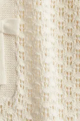 Vestido corto de tejido pointelle color crema, con cuello redondo, mangas cortas y abertura frontal con dos moños decorativos.