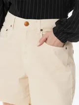 Short de sarga de algodón en color beige claro, con diseño de tiro alto y corte holgado. Presenta cinco bolsillos, pretina con trabillas, cierre frontal con cremallera y botón, y dobladillo con acabado deshilachado.