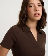 Blusa de punto acanalado (rib) color marrón oscuro, con cuello polo, escote en V y manga corta.