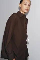 Camisa marrón de algodón con cuello solapa, manga larga con puños abotonados, bolsillo de parche en el pecho y cierre frontal con botones.