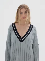 Buzo tejido oversized color celeste, con cuello en V y ribetes negros y blancos. Presenta mangas largas con diseño de trenzas y puños y dobladillo acanalados en color negro.