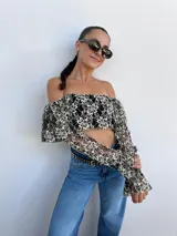 Top corto negro con diseño de encaje floral en blanco, escote bardot y mangas largas acampanadas.